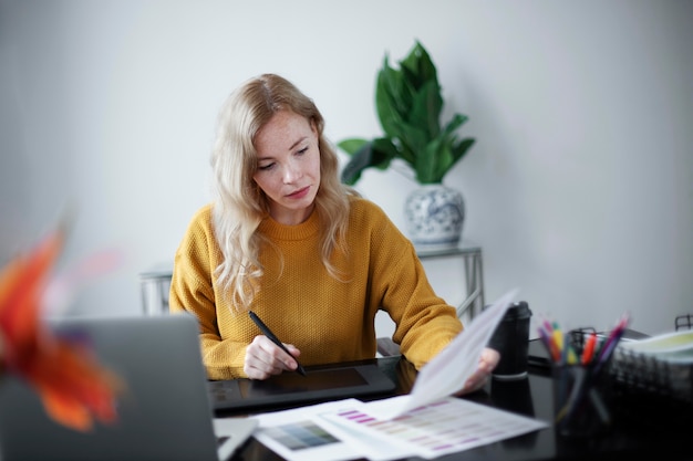 Foto vrouwelijke logo-ontwerper werkt aan haar tablet die is aangesloten op een laptop