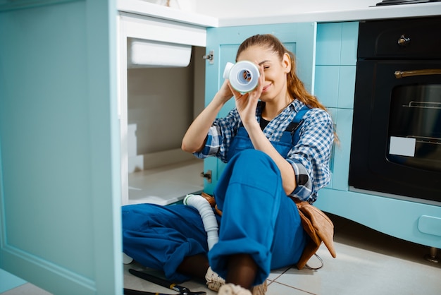 Vrouwelijke loodgieter in uniform liggend op de vloer in de keuken, bovenaanzicht. klusjesvrouw met gereedschapstas reparatie gootsteen, sanitair service aan huis