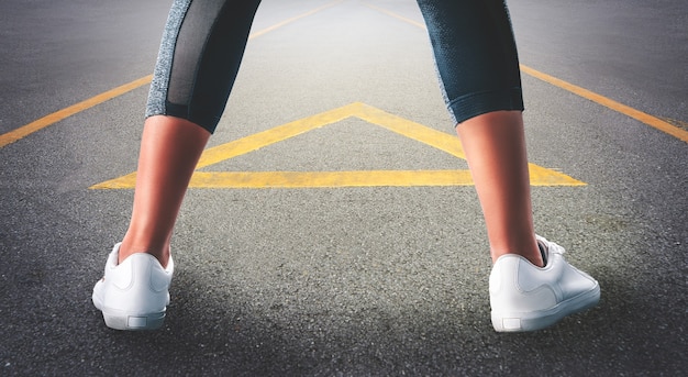 Vrouwelijke loper benen spreiden zich klaar om te trainen op de weg met de richting van de pijl.