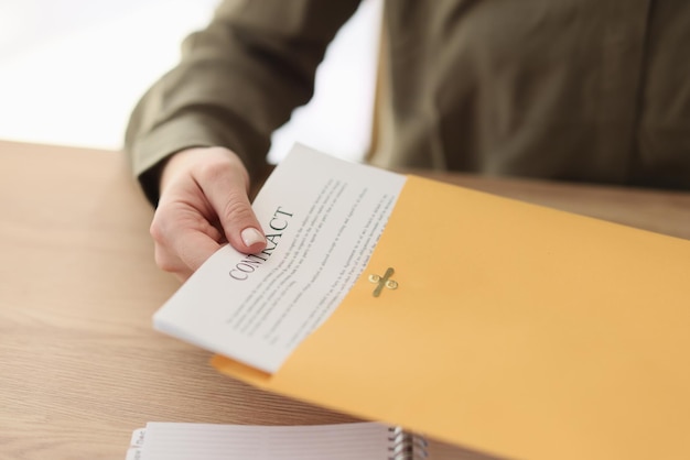 Vrouwelijke manager stopt contractpapieren in gele map zittend aan houten tafel vrouw redt