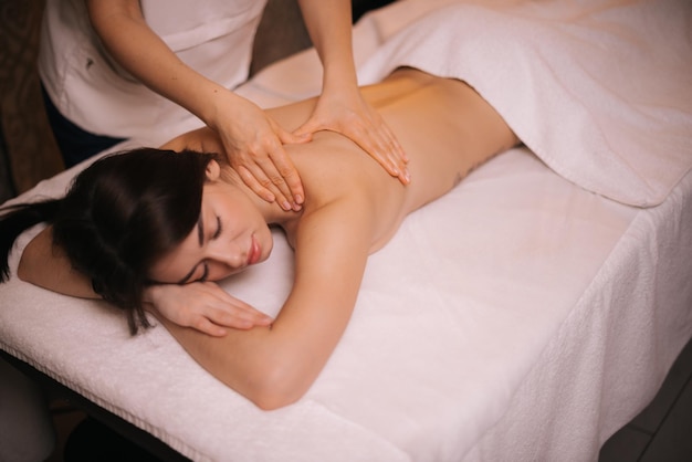 Vrouwelijke masseuse doet schouder- en rugmassage aan jonge vrouw in spa centrum close-up Mooi meisje met perfecte huid krijgt ontspannende massage Concept van professionele massage Concept van lichaamsverzorging