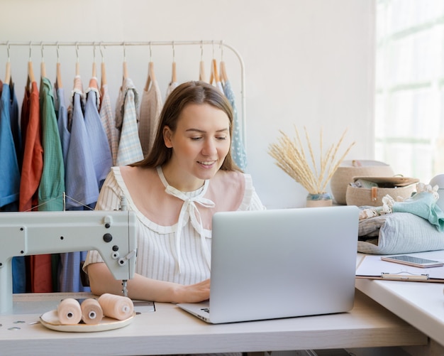 Vrouwelijke modeontwerper die online kledingontwerp maakt terwijl ze op de werkplek zit met naaien