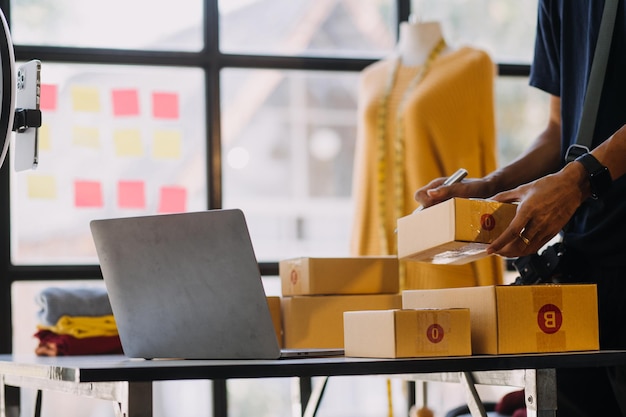 Vrouwelijke modeontwerper kijkt naar tekeningen en schetsen die aan de muur zijn bevestigd achter haar bureau Studio is zonnig Persoonlijke computer Kleurige stoffen Naaldwerkstukken zijn zichtbaar