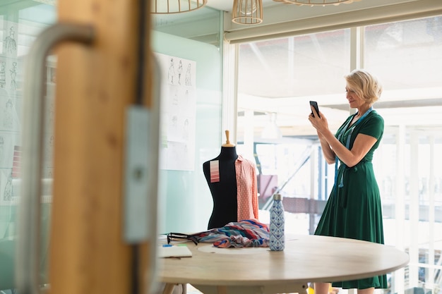 Foto vrouwelijke modeontwerper met een mobiele telefoon in de ontwerpstudio