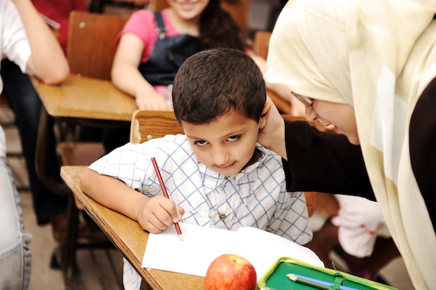 Vrouwelijke moslimleraar helpt een kleine leerling in de klas