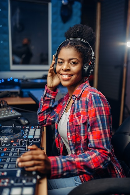 Vrouwelijke muzikant in koptelefoon op het bedieningspaneel van de afstandsbediening in audio-opnamestudio.