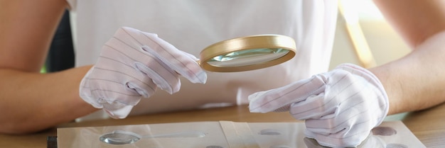 Vrouwelijke numismaticus in handschoenen onderzoekt haar verzameling munten aan tafel close-up van vrouw op zoek