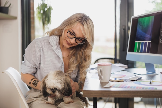 Vrouwelijke ontwerper die plezier heeft met haar hond terwijl ze in haar thuisstudio werkt.