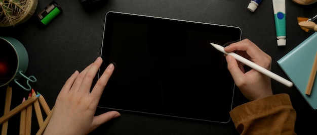 Vrouwelijke ontwerper puttend uit digitale tablet met stylus pen op donkere werktafel met tekengereedschappen