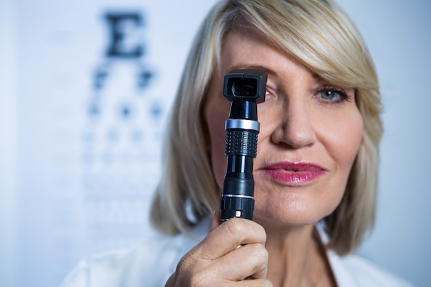 Vrouwelijke optometrist die door oftalmoscoop kijkt