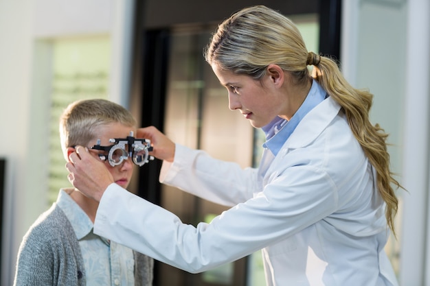 Vrouwelijke optometrist die jonge patiënt met phoropter onderzoekt