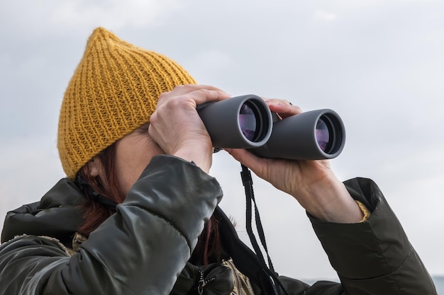 Vrouwelijke ornitholoog birdman kijkt naar vogels met een verrekijker op een vuil grindweg tegen de achtergrond van een stormachtige lucht