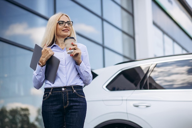 Foto vrouwelijke oude autodealer die koffie drinkt buiten de autoshowroom