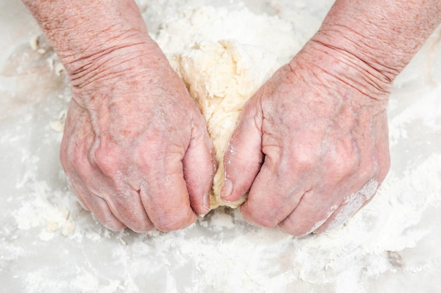 Vrouwelijke oude handen kneden het deeg op een tafel, close-up