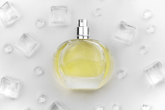 Vrouwelijke parfum gele fles Objectieve foto van parfumfles in ijsblokjes en water op witte tafel Uitzicht van bovenaf Mockup product foto concept van versheid