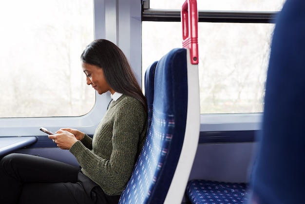 Vrouwelijke passagier zit in de trein en kijkt naar mobiele telefoon