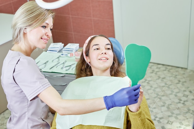 Vrouwelijke patiënt die tanden in de spiegel controleert. Jong meisje op het kantoor van de tandarts. Nieuwe tandheelkundige implantaten.