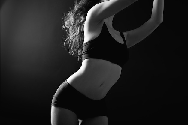 Vrouwelijke perfectie. Lichaamsverzorging. Flexibele vrouw torso silhouet in zwarte atletische ondergoed geïsoleerd op donker.