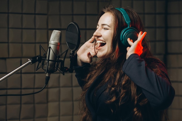 Vrouwelijke persoon neemt POP-nummer op in de opnamestudio Zangeres emotioneel gebarend met haar handen Geluiddichte ruimte voor professionele zangopname