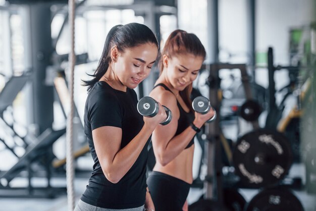 Vrouwelijke persoonlijke trainer die vrouw helpt die oefeningen in de gymnastiek doet.