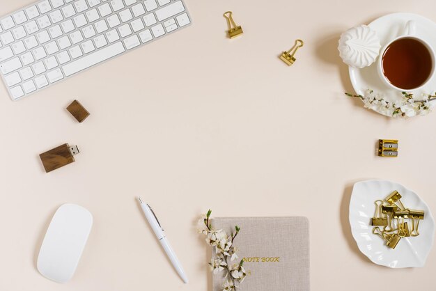 Vrouwelijke platte werkruimte met laptop, kopje thee, marshmallow en bloemen op beige tafel