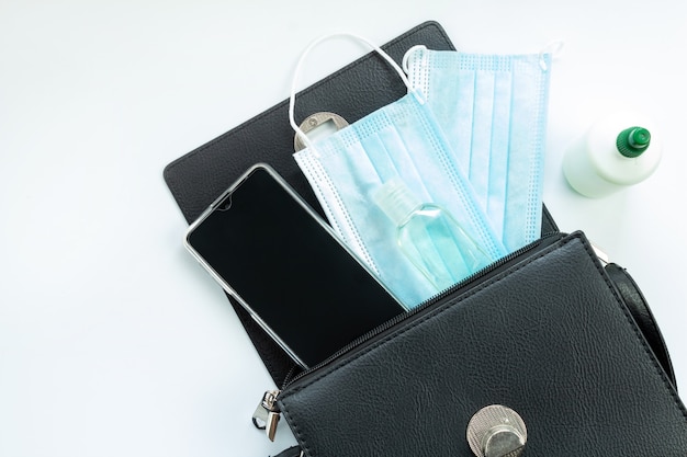 Vrouwelijke portemonnee met telefoon, antiseptisch, medisch masker en op een witte achtergrond, bovenaanzicht, geïsoleerd