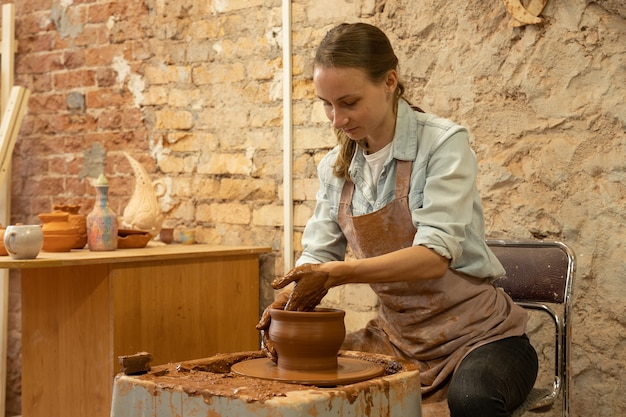 Vrouwelijke pottenbakker beeldhouwt een aarden pot de beeldhouwer werkt met klei op een pottenbakkersschijf en aan een tafel