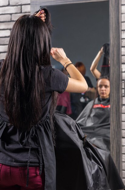 Vrouwelijke professionele kapper die nat haar van een jonge brunette vrouw kamt terwijl ze in een leunstoel in de schoonheidssalon zit