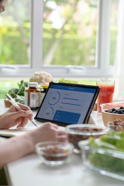 Vrouwelijke professionele voedingsdeskundige die werkt en gegevens controleert van een laptop met een verscheidenheid aan fruit, noten, groenten en voedingssupplementen op tafel