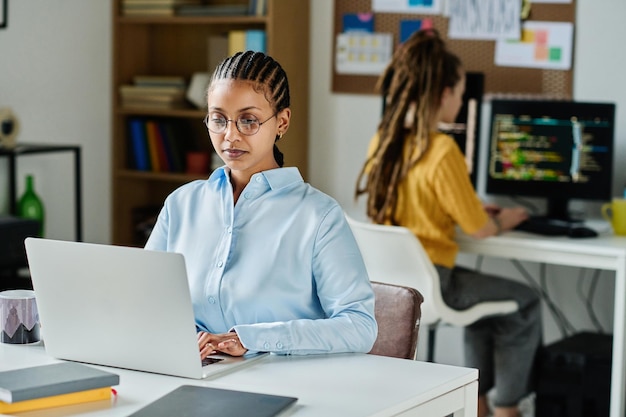 Vrouwelijke programmeur die online op laptop werkt terwijl ze op haar werkplek op kantoor zit