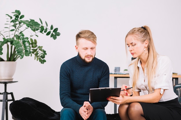 Foto vrouwelijke psycholoog die klembord tonen aan zijn mannelijke patiënt in de kliniek