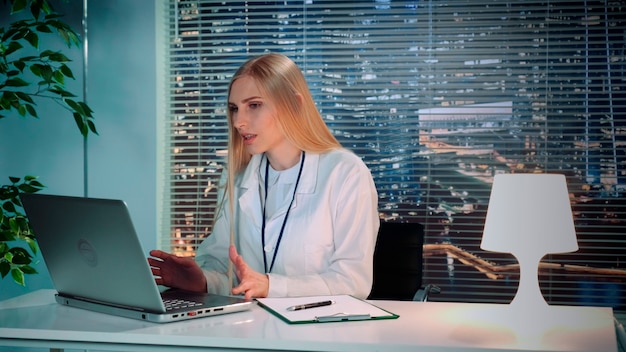 Vrouwelijke psycholoog in witte jas die online videoconsult maakt met patiënt op computerzitting