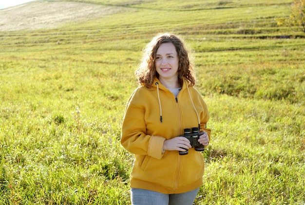 Vrouwelijke reiziger die een verrekijker in geel veldlandschap bekijkt. Reis en verken concept.