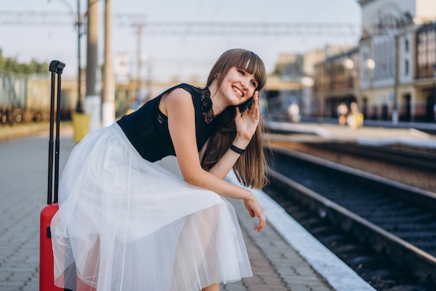 Foto vrouwelijke reiziger met de rode trein van het kofferwachten op station