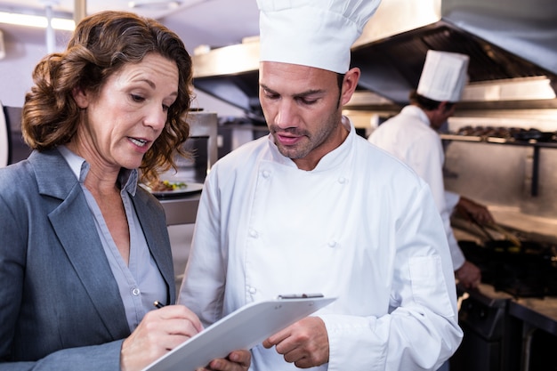 Vrouwelijke restaurantmanager die op klembord schrijft terwijl het interactie aangaan met chef-kok