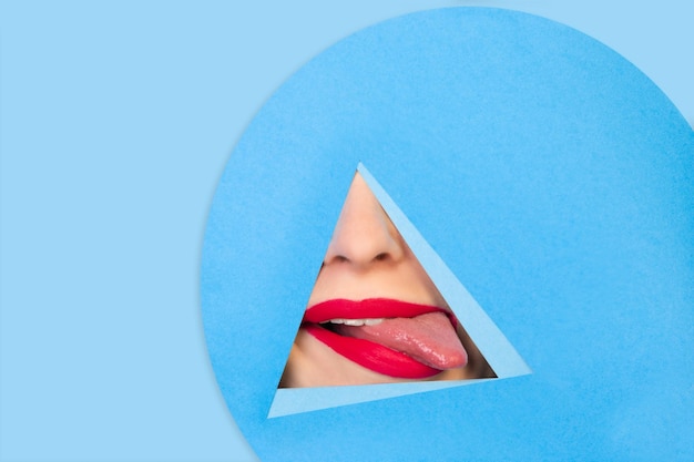 Vrouwelijke rode lippen die door driehoek op blauwe achtergrond gluren