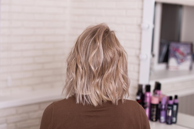 Vrouwelijke rug met krullend ombre blond haar in een kapsalon