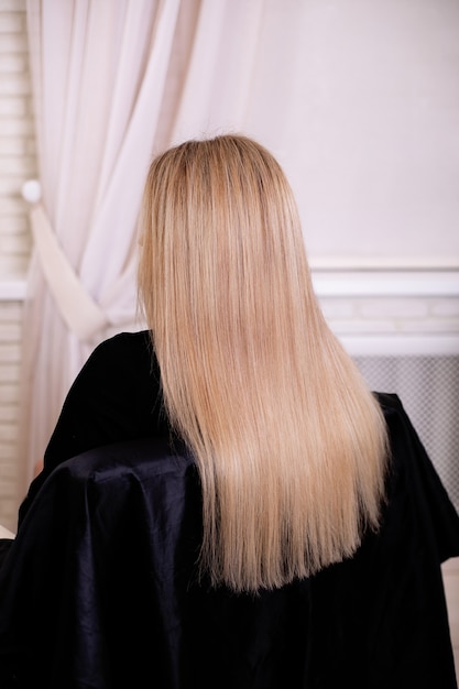Vrouwelijke rug met lang, recht, blond haar, in de kapsalon