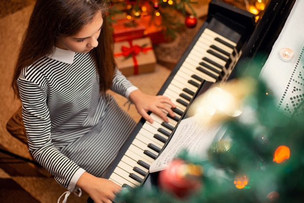 Vrouwelijke schoolmeisje in zwart-wit gestreepte jurk piano spelen met kerstcadeautjes op de achtergrond