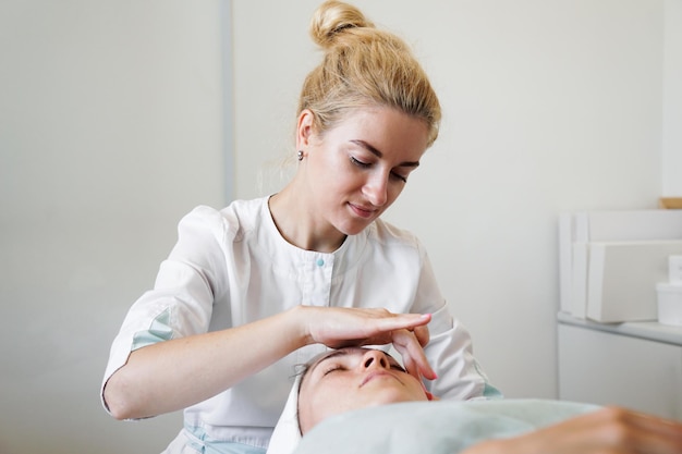 Vrouwelijke schoonheidsspecialiste die haar vrouwelijke cliënt gezichtsmassage doet in een schoonheidskliniek