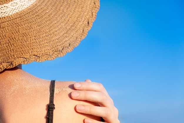 Foto vrouwelijke schouder bedekt met zand op heldere blauwe achtergrond.