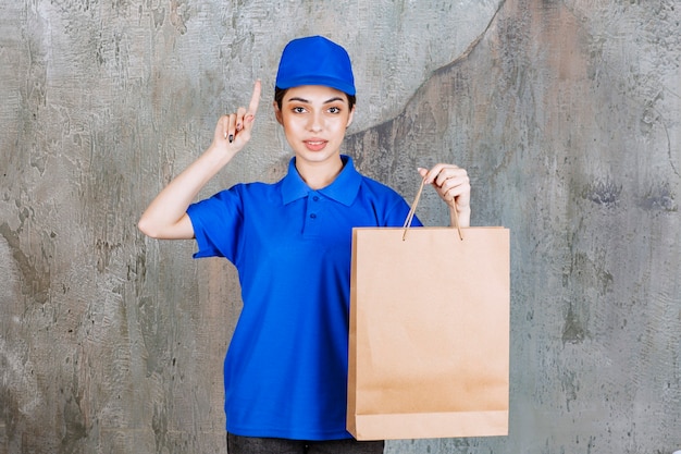 Vrouwelijke serviceagent in blauw uniform met een kartonnen boodschappentas en denkt een idee te hebben.