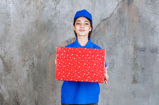 Vrouwelijke serviceagent in blauw uniform met een rode geschenkdoos met witte stippen erop.