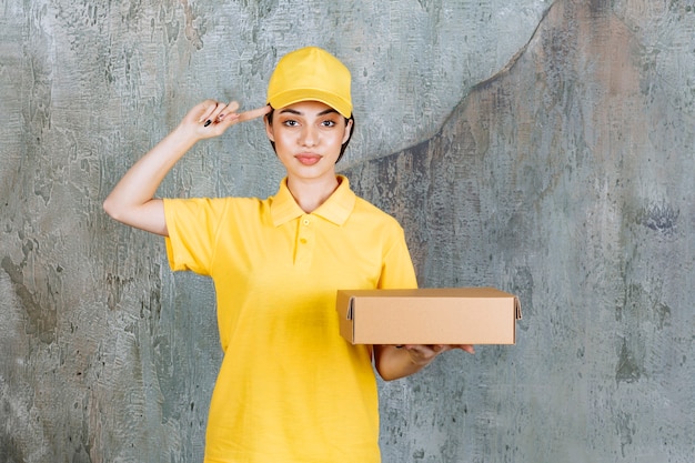 Vrouwelijke serviceagent in geel uniform met een kartonnen doos en ziet er verward en attent uit.