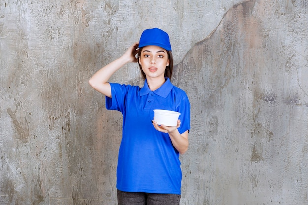 Foto vrouwelijke servicemedewerker in blauw uniform met een plastic kom en ziet er verward en attent uit of heeft een goed idee.