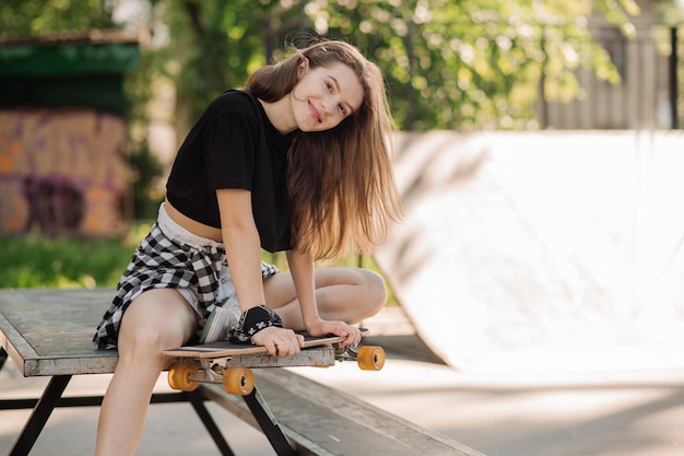 Vrouwelijke skater met een skateboard zit en rust in het skaterspark