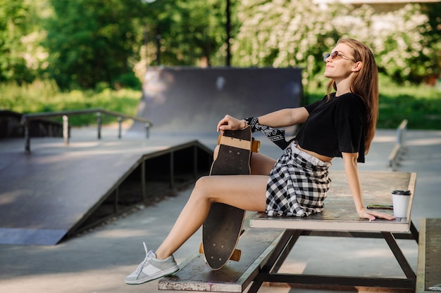 Vrouwelijke skater met een skateboard zit en rust in het skaterspark