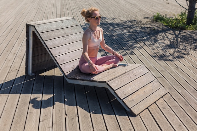 Vrouwelijke sportman zittend in yoga meditatie pose met gesloten ogen en met gekruiste benen op houten terras