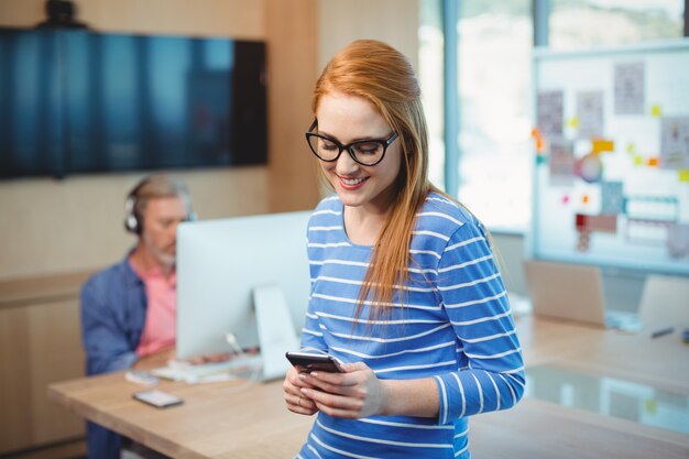 Vrouwelijke stafmedewerker die mobiele telefoon in bureau met behulp van