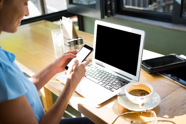 Vrouwelijke stafmedewerker met behulp van mobiele telefoon in café